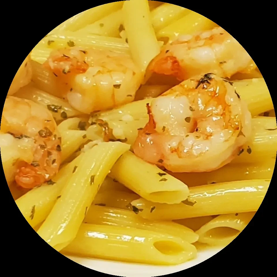 Close-up of penne pasta with grilled shrimp and green herbs.