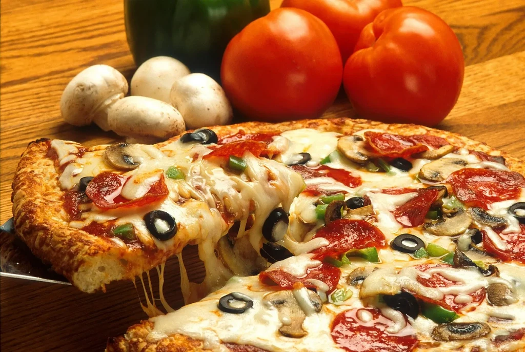 Pizza slice lifting with cheese pull, pepperoni, mushrooms, and vegetables.