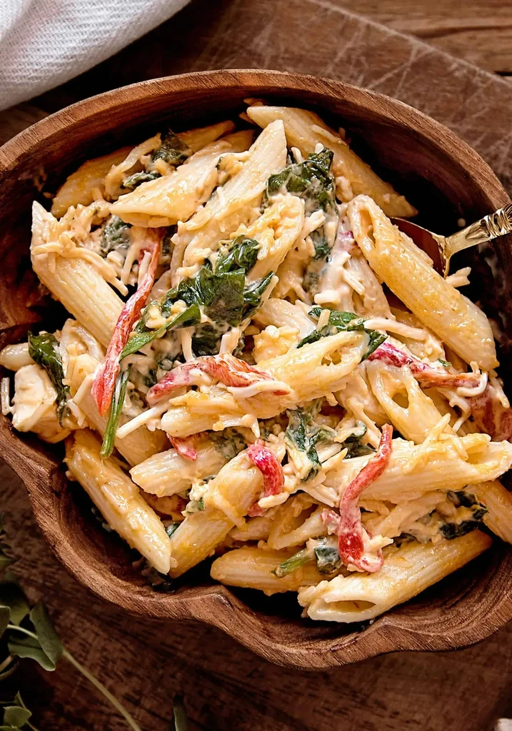 Overhead penne pasta in creamy sauce with spinach, bell pepper, wooden bowl.