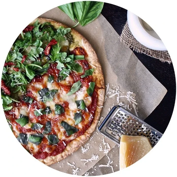 Rustic pizza with two halves: arugula, sun-dried tomatoes, mozzarella, basil.