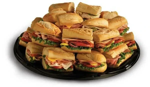 Black platter piled with mini deli sandwiches on crusty rolls.