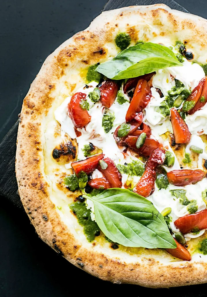 Overhead gourmet pizza with strawberries, pesto, pistachios, and basil.