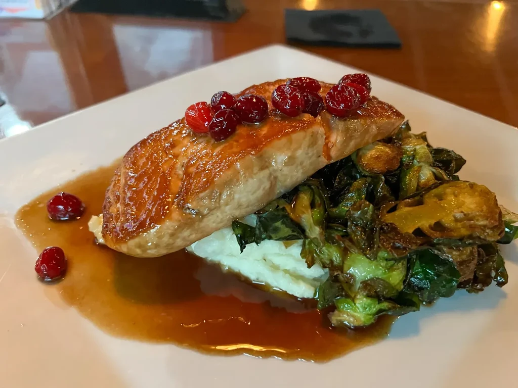 Pan-seared salmon, mashed potatoes, brussels sprouts with sauce and cranberries.