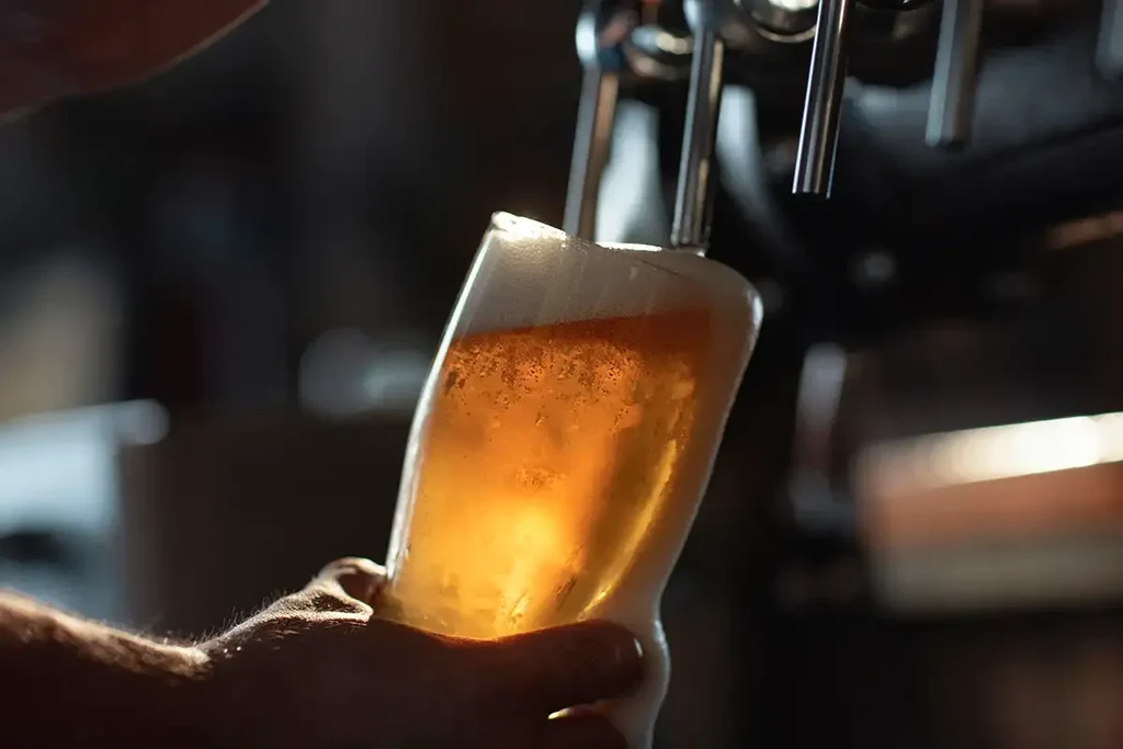Amber beer with frothy head pours into a glass from a tap.