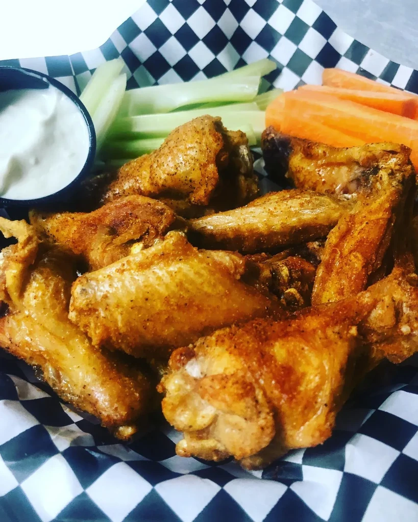 Golden-brown chicken wings, white dip, celery, and carrots in a basket.