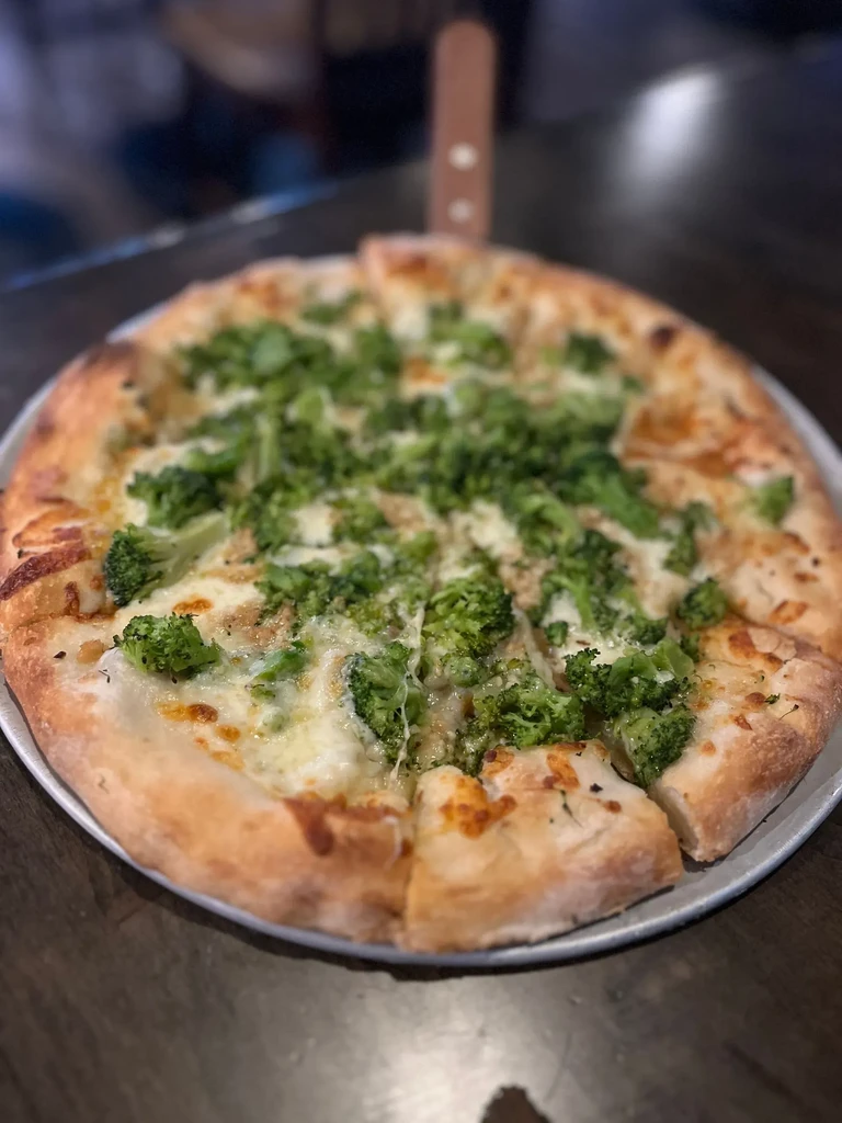 Freshly baked pizza with melted white cheese and bright green broccoli, sliced.