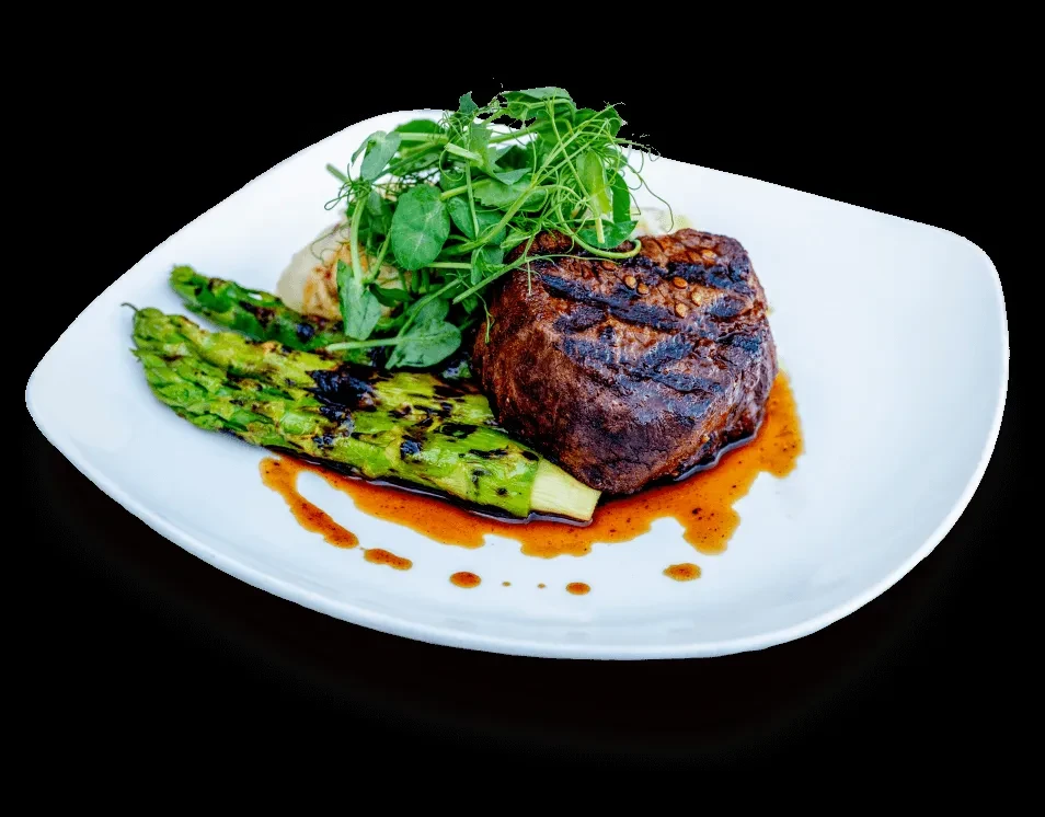Plated grilled steak, asparagus, and microgreens with drizzled sauce.