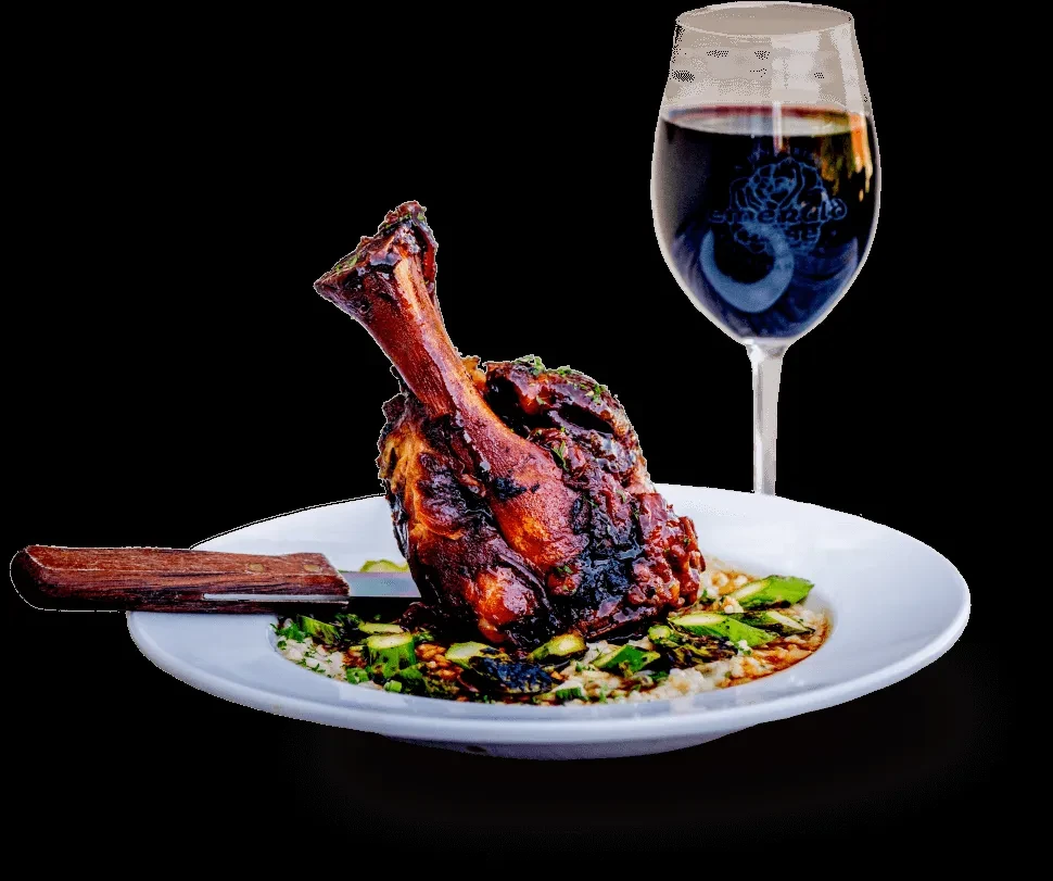 Dark-glazed meat shank, creamy base, vegetables, red wine, and knife.