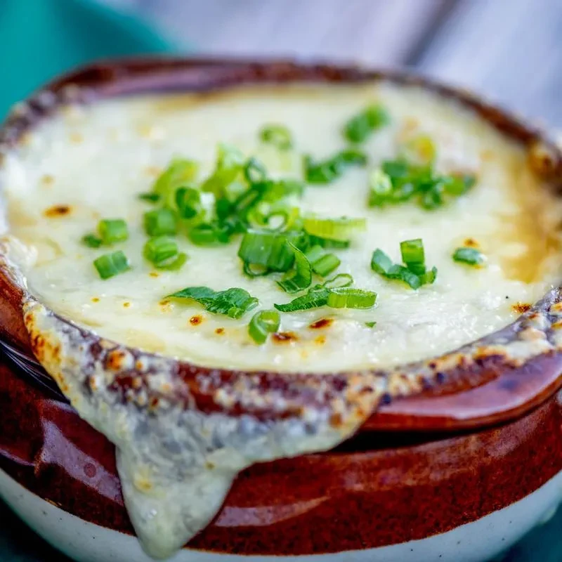 Rustic bowl of French onion soup topped with melted cheese and chives.