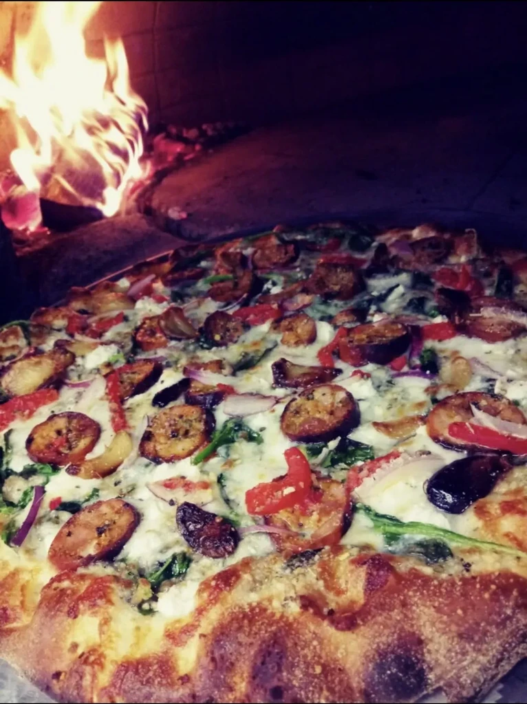 Pizza with cheese, sausage, vegetables baking in a wood-fired oven.