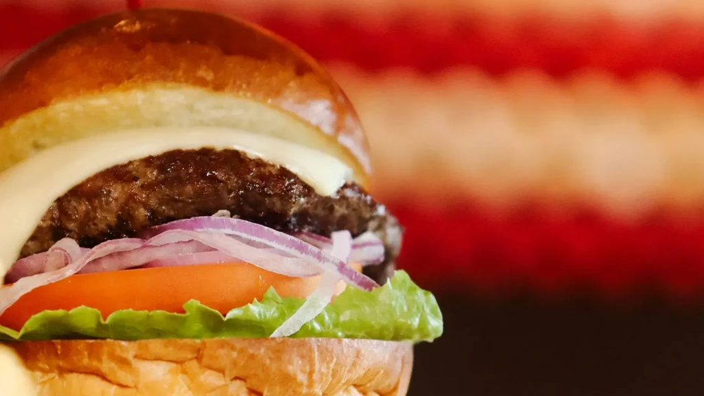 Layered burger: bun, melted cheese, beef patty, onion, tomato, lettuce.