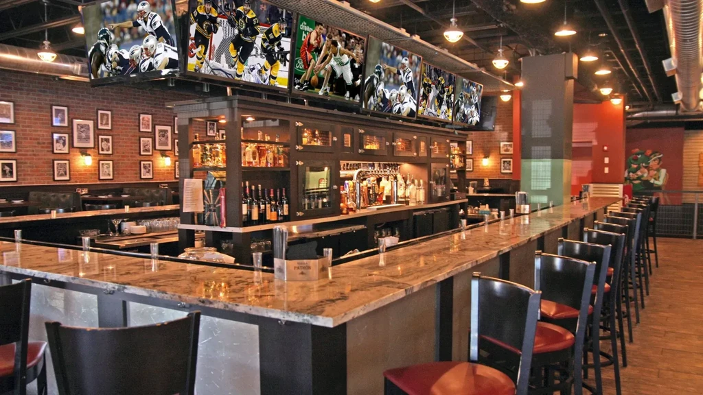 Spacious sports bar interior with a long bar, TVs, and brick walls.