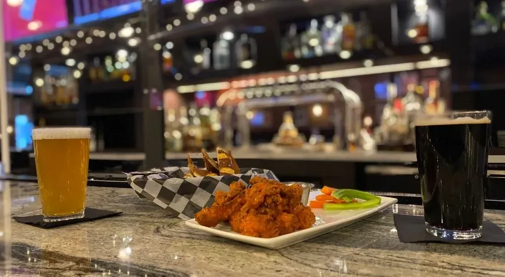 Light and dark beers, buffalo wings, fries on a bar counter.