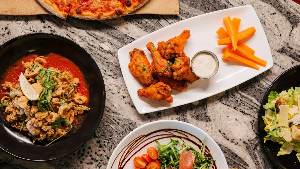 Overhead shot of pizza, chicken wings, calamari, and two diverse salads.