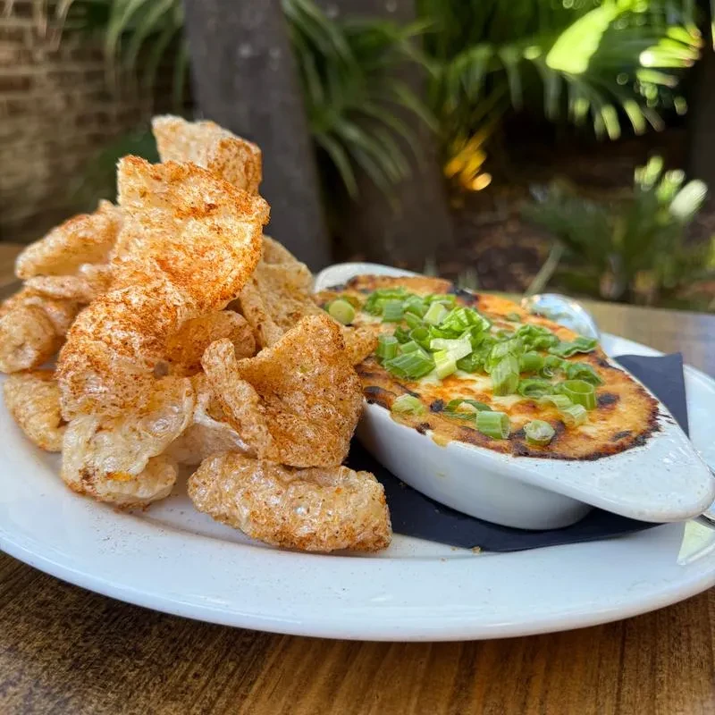 Chicharrons and baked cheesy dip with green onions on a wooden table.