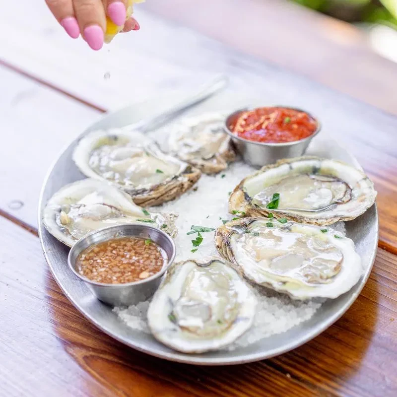Hand squeezing lemon over fresh oysters on ice with sauces.