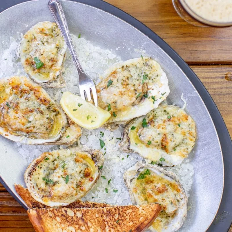 Platter of six baked oysters with cheesy gratin, herbs, and lemon.