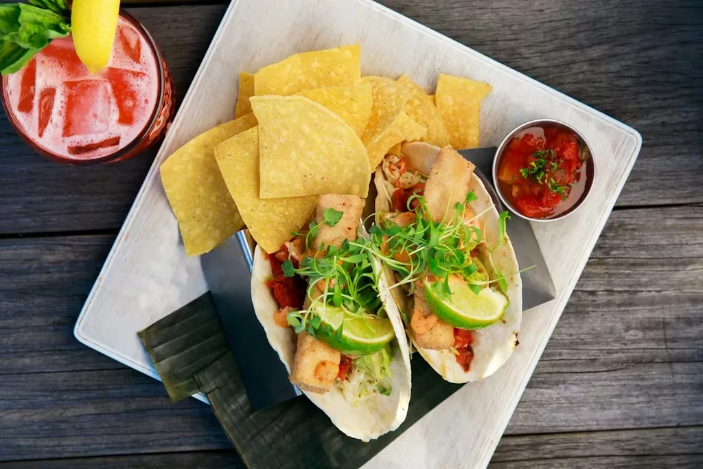 Fish tacos, chips, salsa, and a red cocktail on a serving board.