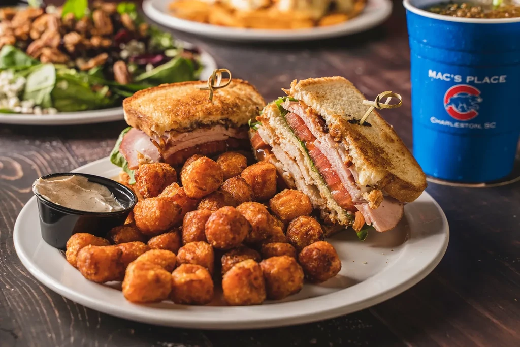 A club sandwich with tater tots, dipping sauce, and Mac's Place cup.