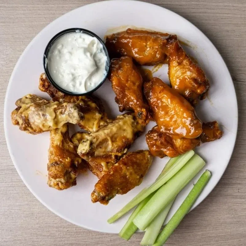 Two kinds of chicken wings, dip, and celery on a white plate.