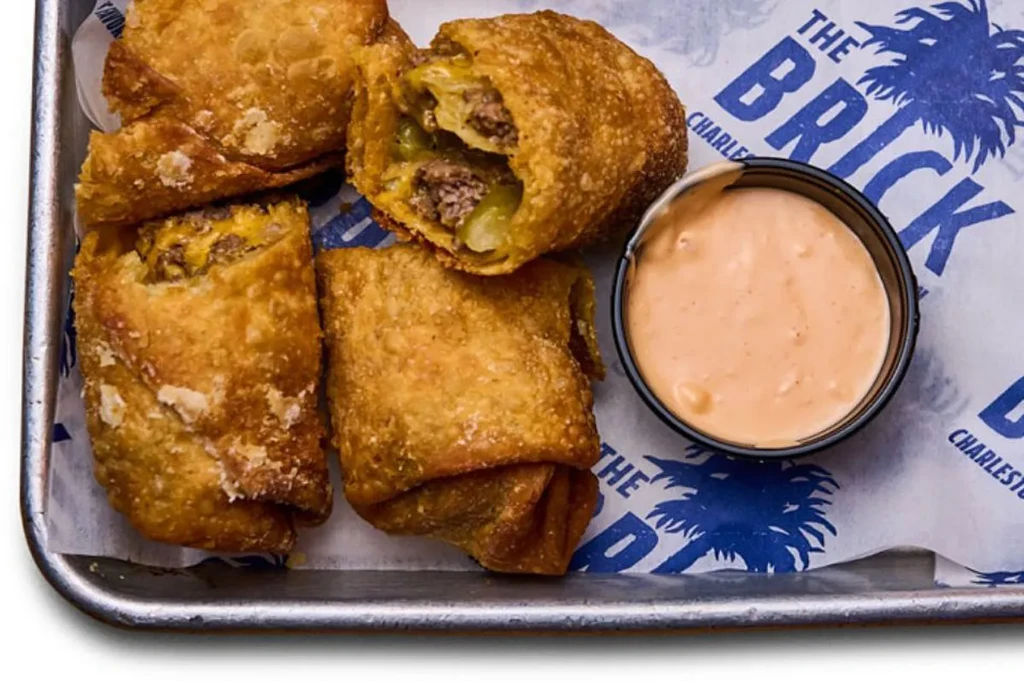 Crispy fried rolls filled with meat, cheese, dipping sauce, on branded paper.