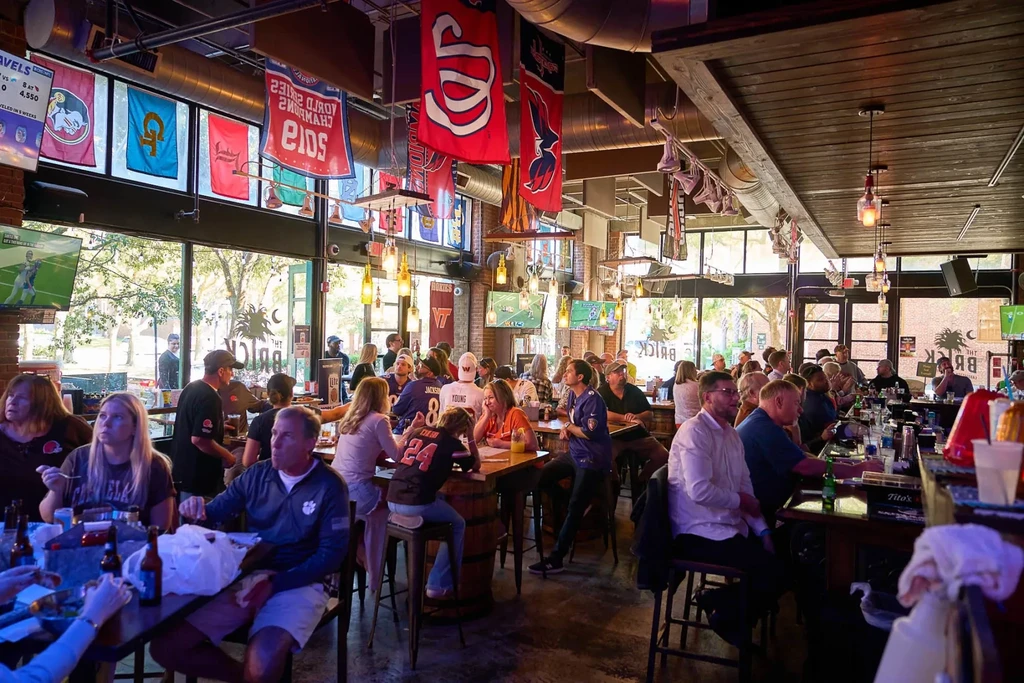 Crowded sports bar interior with patrons eating, drinking, watching sports.