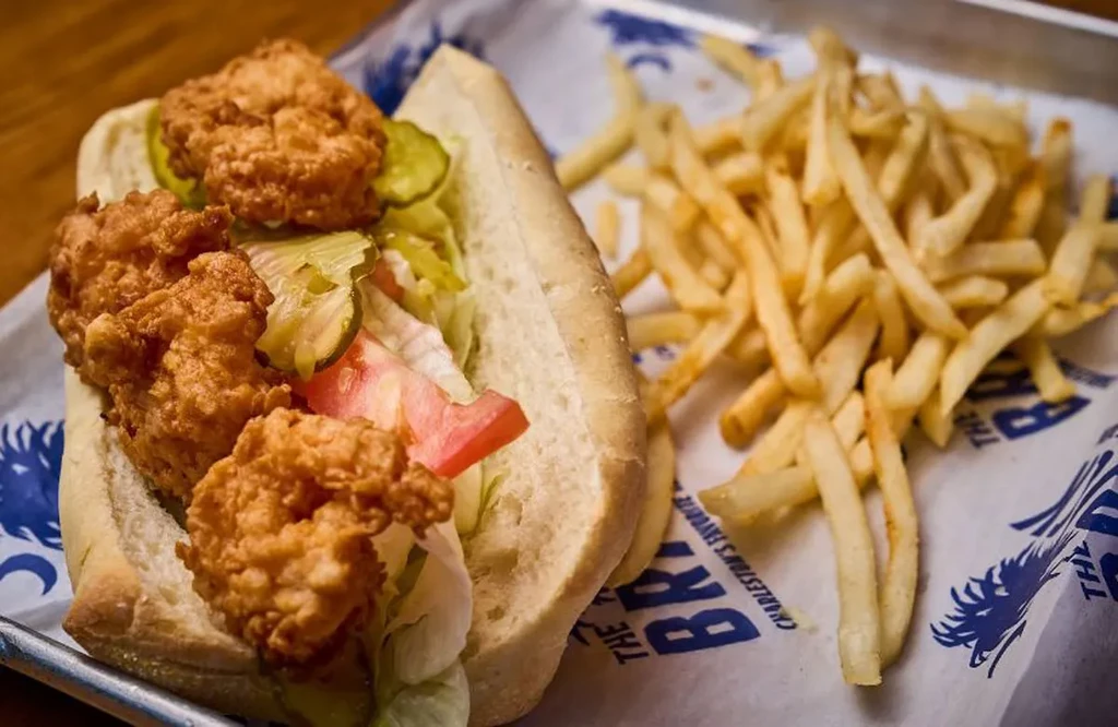 A fried shrimp po'boy, fries, and patterned tray with Charleston branding.
