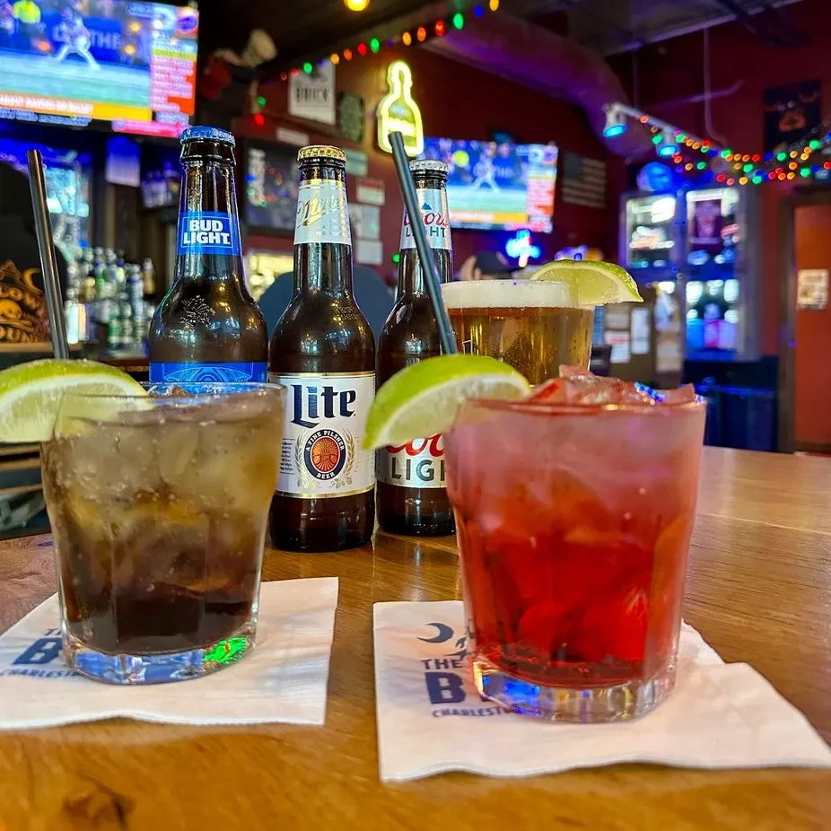 Cocktails and beer bottles on a wooden bar in a lively bar.