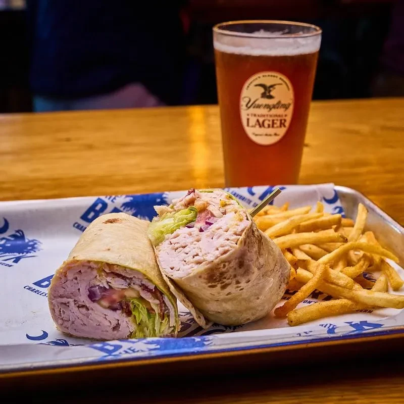 A cut wrap, french fries, and Yuengling beer on a metal tray.