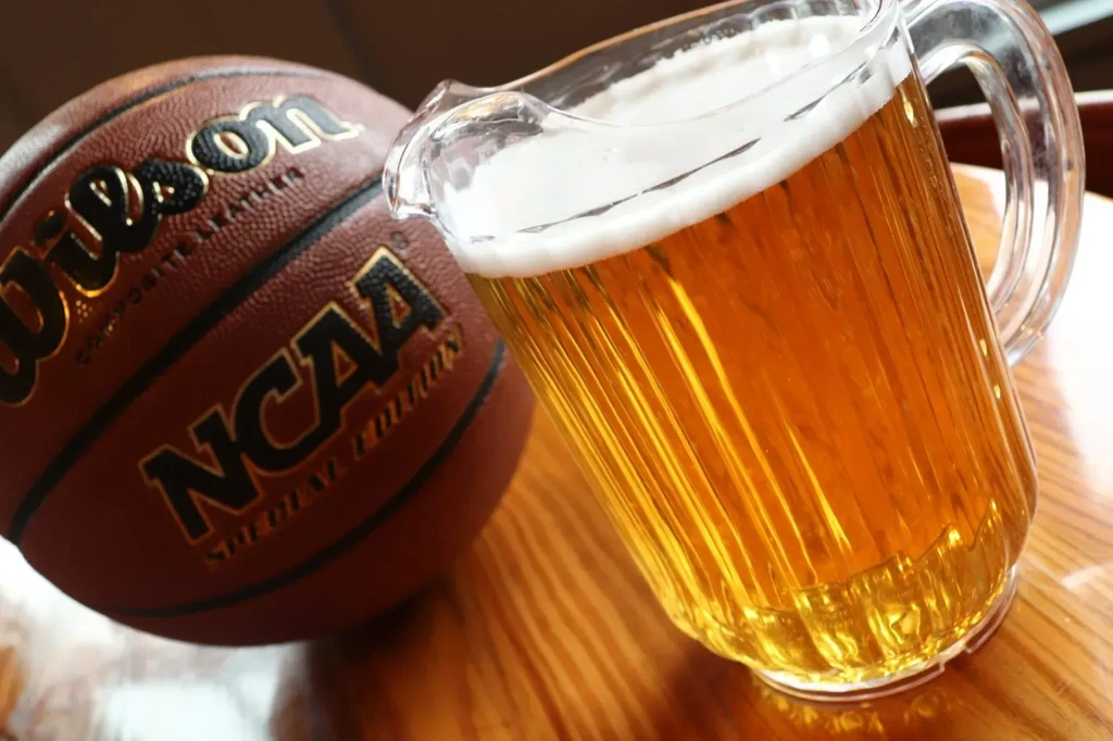 Golden beer pitcher next to a Wilson NCAA basketball on wood.