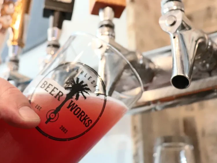 Hand fills Beer Works logo glass with reddish beverage from tap.