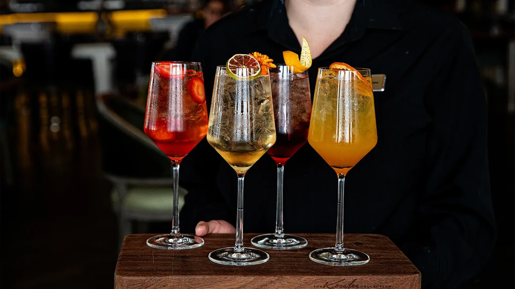 Four vibrant cocktails on a tray, held by a server.