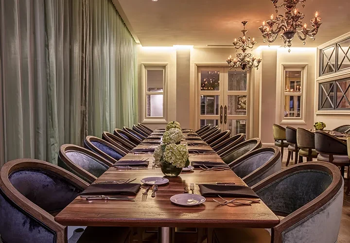 Luxurious dining room with long wooden table, hydrangeas, and plush chairs.