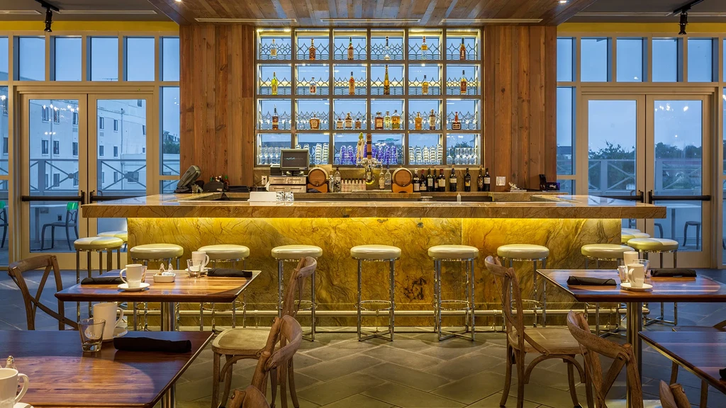 Modern restaurant interior: illuminated yellow-gold marble bar, bottles on shelves.
