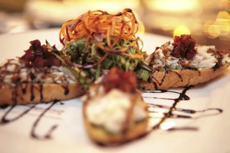 Three crostini with creamy topping, balsamic glaze, and vegetable garnishes.