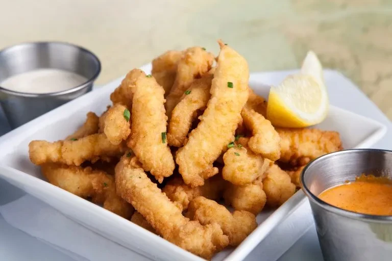 Golden-brown fried food with green herbs, two sauces, and lemon.