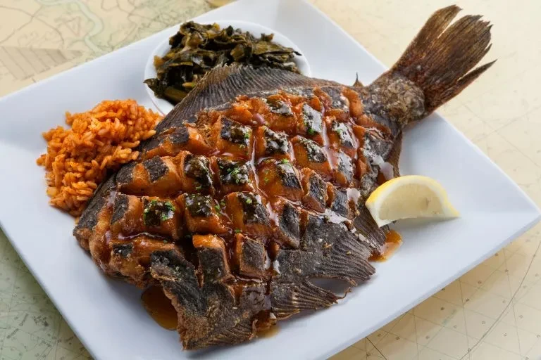 Crispy fried whole fish with sauce, orange rice, greens, and lemon.