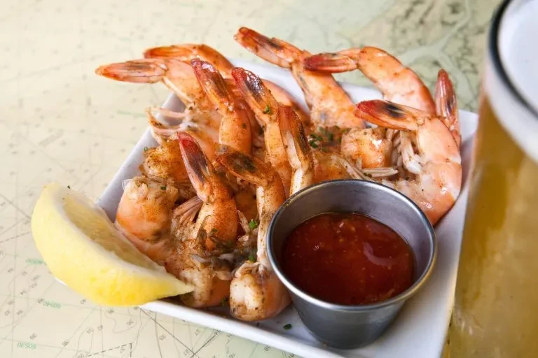 Seasoned cooked shrimp, lemon, dipping sauce, and beer on a nautical chart.