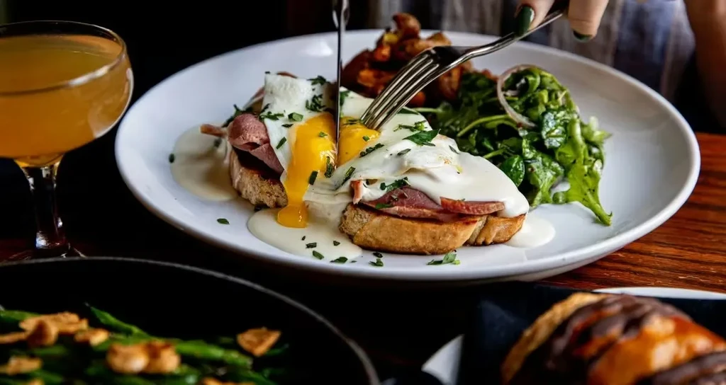 Hands cut into a breakfast dish, a bright runny yolk drips.