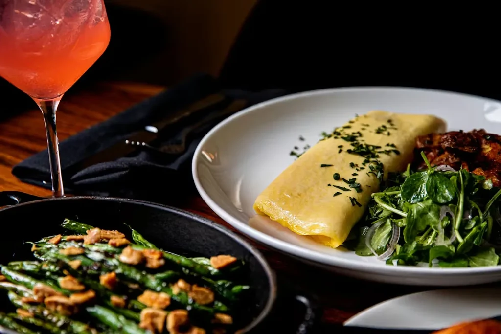 A sophisticated meal with omelet, green beans, salad, potatoes, and pink cocktail.