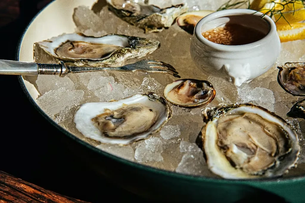 Opened oysters and clams on ice with sauce, lemon, and fork.