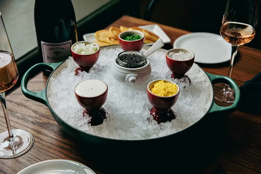 Caviar service: black caviar on ice with garnishes, blini, and wine.