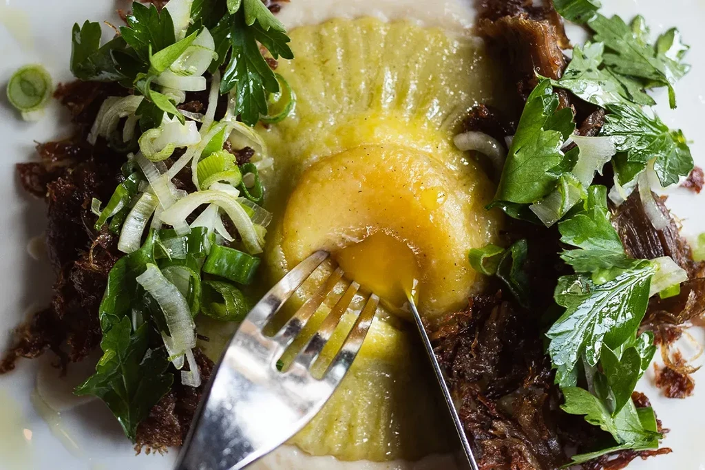 Close-up of gourmet pasta dish with runny egg yolk and fresh herbs.
