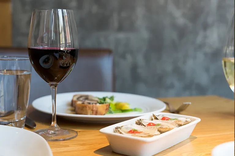 Close-up of three oysters, red wine, and water on a restaurant table.
