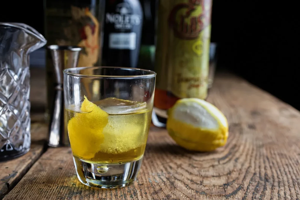 Chilled yellow cocktail with lemon peel and ice on rustic wood.