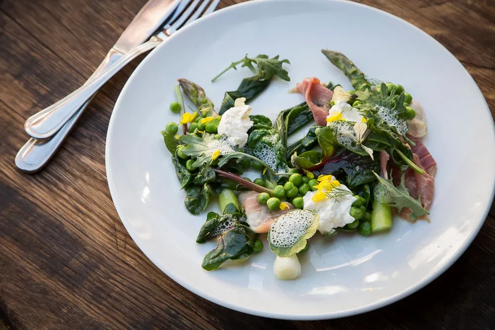 Plated gourmet salad with asparagus, prosciutto, cheese, and edible flowers.