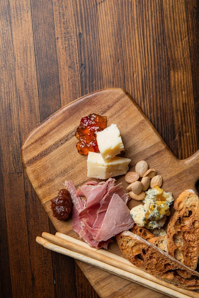 Cutting board with cheeses, cured meats, bread, jams, and almonds.