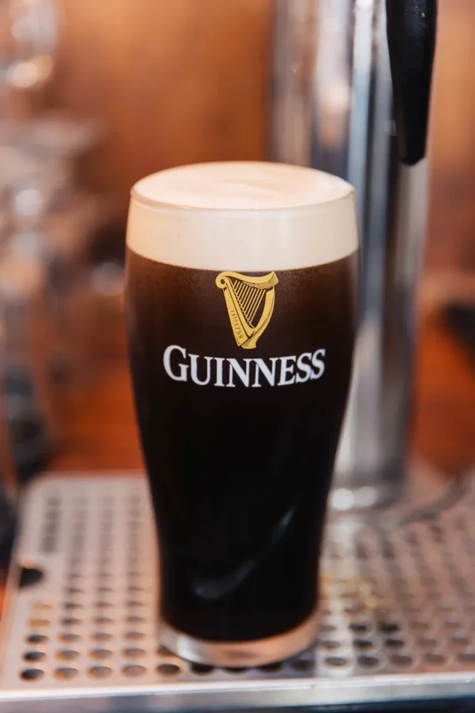 Guinness pint with logo, creamy head, on a bar drip tray.