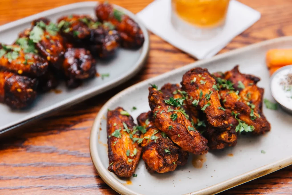 Plates of deep reddish-brown chicken wings with herbs, dipping sauce, carrots.