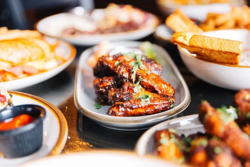 Plate of dark-glazed chicken wings with herbs and blurred side dishes.